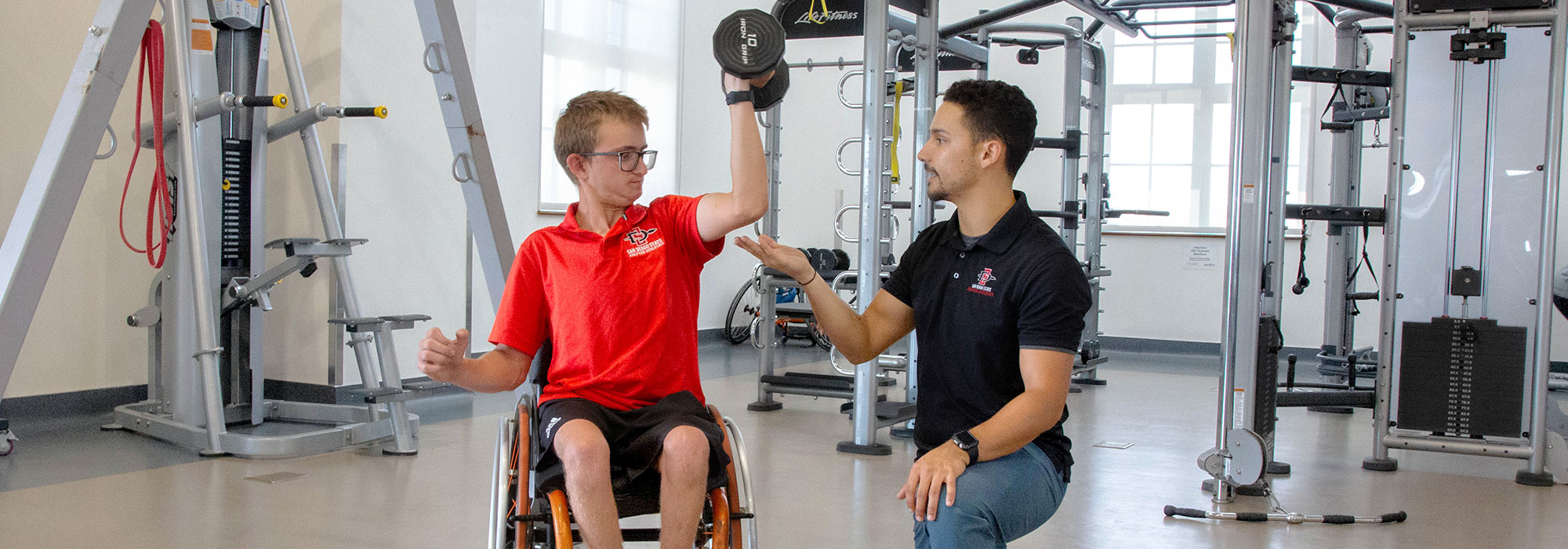 Adaptive Athletics - Young man in weelchair instructed technique on working out with a dumbell